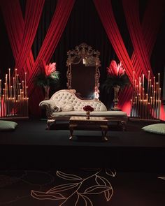 a couch sitting on top of a stage covered in red drapes and lit candles