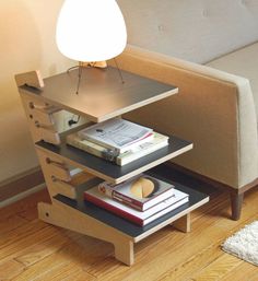 a table with books and a lamp on it in front of a white couch next to a wooden floor