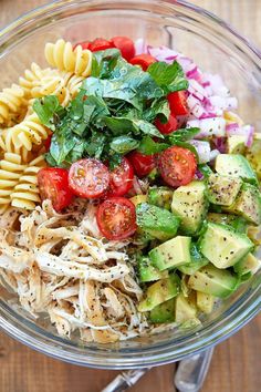 a glass bowl filled with pasta salad on top of a wooden table