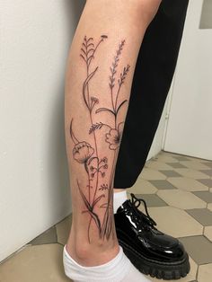 a woman's leg with flowers on it and a black shoe in the foreground