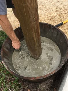 a man is pouring water into a bucket with a wooden pole in the back ground