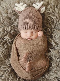 a baby is wearing a knitted deer hat and sleeping on a pile of carpet