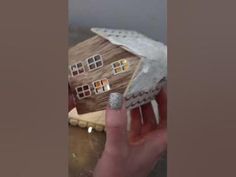 a hand is holding a small house made out of wood and paper with nails on it