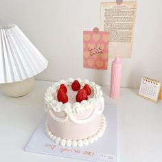 a white cake with strawberries on top sitting on a table next to a calendar