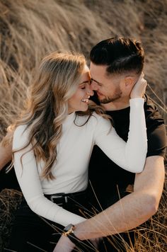 a man and woman are sitting in the tall grass with their arms around each other