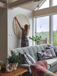 a woman standing on top of a couch in a living room next to a window