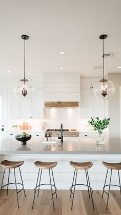 three stools are sitting at the bar in this modern kitchen with white cabinets and wood flooring