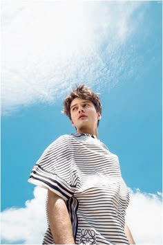 a man standing under a blue sky with his hair in the air and wearing a striped shirt