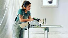 a woman is using a circular saw to cut wood with a power drill and headphones on