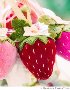 three stuffed strawberries are hanging from a string with flowers and leaves on them,