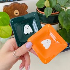 a person holding two small square plates with ghost faces on them in front of some potted plants