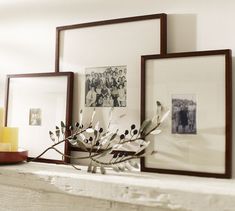 three framed pictures on a mantel with flowers and candles in the foregrounds