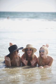 three girls in the water with hats and sunglasses on their heads, one is smiling