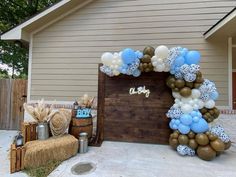 a balloon arch with blue, white and gold balloons in front of a house for a baby's first birthday