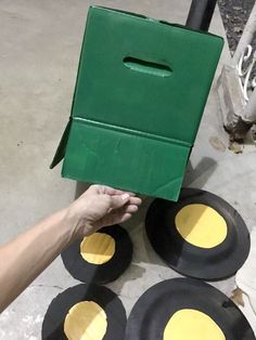 a person holding up a green box with yellow circles on the sides and four black plates around it