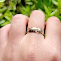 a person's hand with a gold and silver wedding ring on it, in front of some plants