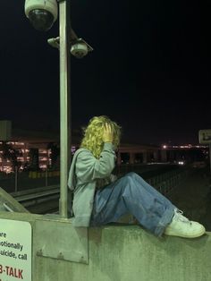 a man sitting on the side of a wall next to a street light at night