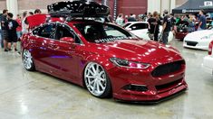 a red car is parked in a showroom with people looking at the cars on display