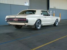 an old white car parked in front of a garage door on the side of a road