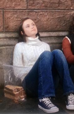 a woman sitting on the ground next to a brick wall with her head in a plastic bag