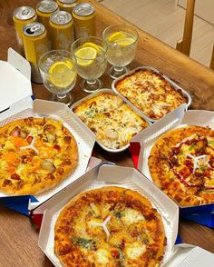 four pizzas in boxes on a table with glasses of beer and drinks behind them