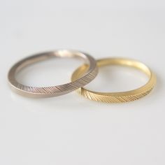 two gold wedding bands sitting next to each other on a white surface with one ring in the middle