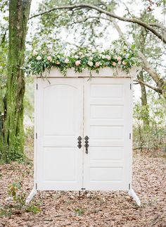 an outdoor wedding ceremony with white doors and flowers on the top, surrounded by trees