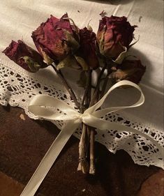 two roses are tied to a piece of lace on a tablecloth with a ribbon