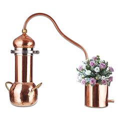 a copper pot with flowers in it next to a metal watering can that is shaped like a flowerpot