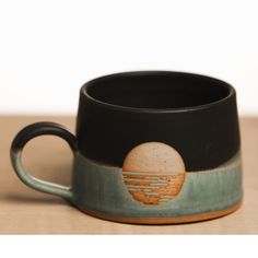 a black and green coffee cup sitting on top of a wooden table