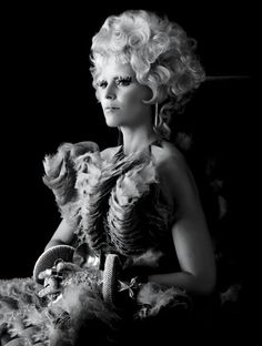 a black and white photo of a woman with feathers on her head, holding a fan