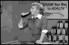 a woman drinking from a bottle while standing in front of a counter