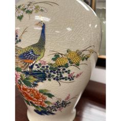 a white vase with flowers and birds painted on it's sides, sitting on a wooden table