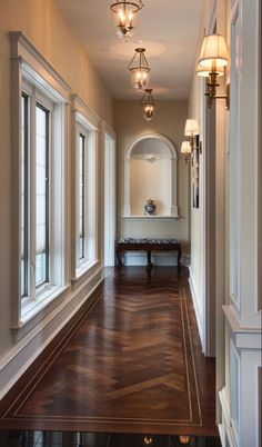 an empty hallway with wood flooring and white trim on the walls, along with two windows