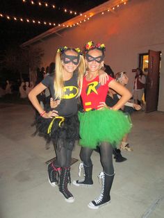 two women dressed up as batman and robinette in costumes at an event with lights strung above them