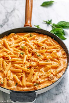 a skillet filled with pasta and sauce on top of a marble counter next to a wooden spoon