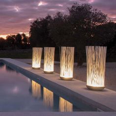 four tall vases sitting next to a pool at night with the sun setting in the background