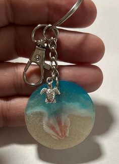 a hand holding a glass keychain with a sea turtle on it's side