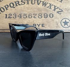 Show off that goth mom pride with these custom-printed glasses! The shape of these sunglasses is a pure classic, but also cool and edgy. The perfect black cat eye with black lenses, but with a white printing of "Goth Mom" on either arm in a gothic font. Slightly oversized and dramatic, just like we like! UV lens protection. Trendy Black Sunglasses For Concerts, Vintage Black Sunglasses For Festival, Black Sunglasses With Gradient Lenses For Festival, Black Tinted Sunglasses For Festival, Black Retro Sunglasses For Festival, Retro Black Sunglasses For Festival, Trendy Halloween Festival Sunglasses, Mom Pride, Gothic Fonts