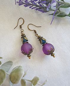 These earrings have a vintage boho flair. They feature 12mm Frosted Purple beads and smaller Frosted Slate Blue Beads accented with layers of petals in Antique Bronze. They dangle approximately 1" from Antique Bronze Earwire. Vintage Teardrop Beaded Earrings For Jewelry Making, Vintage Teardrop Beaded Earrings Nickel Free, Vintage Round Beaded Earrings, Vintage Beaded Teardrop Earrings, Vintage Teardrop Beaded Earrings, Vintage Earrings With Dangling Round Beads, Nickel-free Vintage Teardrop Beaded Earrings, Bohemian Pierced Earrings With Czech Glass, Vintage Nickel-free Beaded Earrings With Round Beads