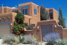 an adobe - style house in the desert surrounded by trees and flowers