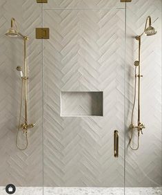 a walk in shower sitting next to a white tiled wall with gold fixtures on it