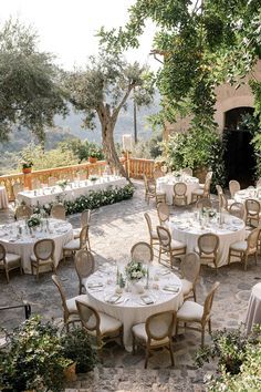 an outdoor dining area with tables and chairs set up for formal function, surrounded by greenery