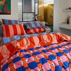 an orange and blue comforter on a bed in a bedroom next to a window