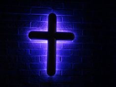 a cross is lit up against a brick wall in the dark with blue light shining on it