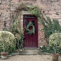 a brick building with a red door and wreath on it's front entrance, surrounded by potted plants