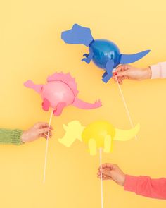 three people are holding colorful paper animals on toothpicks in front of a yellow background