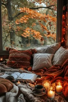 a bed covered in blankets and pillows next to a window with candles on the windowsill