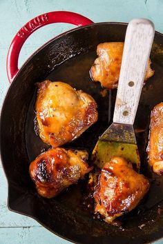 some chicken wings are cooking in a skillet with a spatula on the side