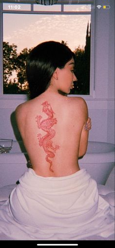 a woman with a dragon tattoo on her back sitting in a bath room next to a toilet